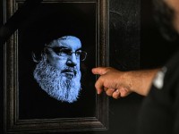 TOPSHOT - A man points to a television set displaying an image of the late leader of Hezbollah Hassan Nasrallah. Picture: AFP.