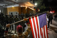 A man holds an American flag as law enforcement officers guard the enterance to ICE headquarters in south Portland, Oregon on Friday. Carlos Barria/Reuters