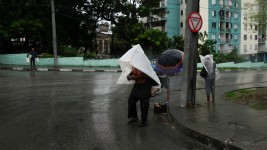 Un homme traverse une rue à Santiago de Cuba et tente de se protéger de la pluie qui tombe dans le sillage du passage de l’ouragan Melissa, le 28 octobre 2025.  Photo : Reuters / Norlys Perez
