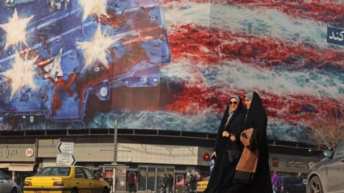 Des Iraniennes marchent devant un panneau anti-américain installé sur la place Enghelab à Téhéran, le 26 janvier 2026 © ATTA KENARE / AFP
