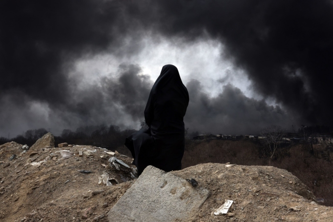 An Iranian woman watches smoke rise from an oil refinery following an airstrike in Tehran. ABEDIN TAHERKENAREH/EPA/SHUTTERSTOCK