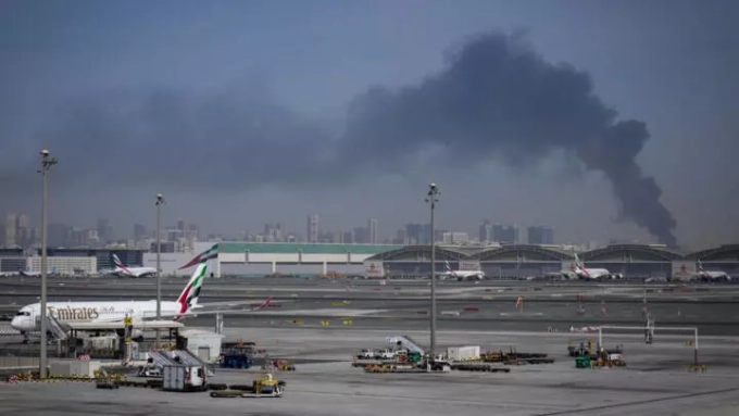 Une colonne de fumée causée par une frappe iranienne est visible à l'arrière-plan de l'aéroport international de Dubaï, le 1er mars 2026. © Altaf Qadri, AP