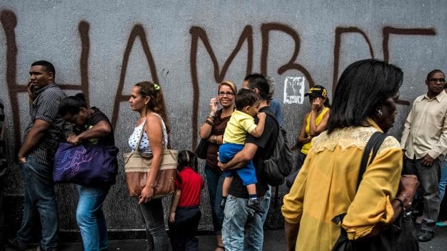 People queue next to a wall with a graffiti reading “Hunger” in Caracas. Picture: Juan Barreto/AFPSource:AFP