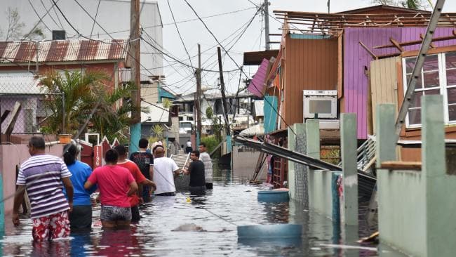 People walk in a flooded street next to damaged houses in Catano town, in Juana Matos, Puerto Rico. Picture: AFPSource:AFP