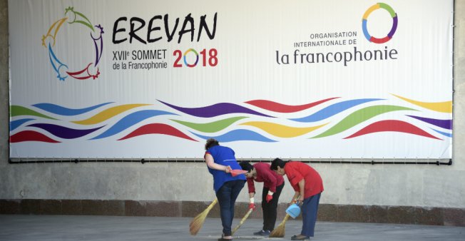 © Karen Minasyan, AFP | Women sweep next to a poster announcing the XVII Francophone countries summit in Yerevan, on October 6, 2018.