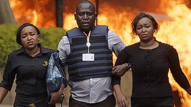 Security forces help civilians flee the scene as cars burn behind, at a hotel complex in Nairobi, Kenya. Picture: APSource:AP