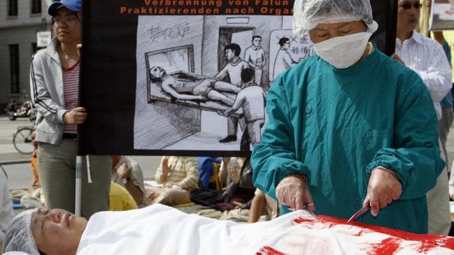 A protester dressed as a Chinese doctor simulates removing organs from another dressed as a Falun Gong practitioner at a protest in Berlin. Picture: Getty ImagesSource:Getty Images