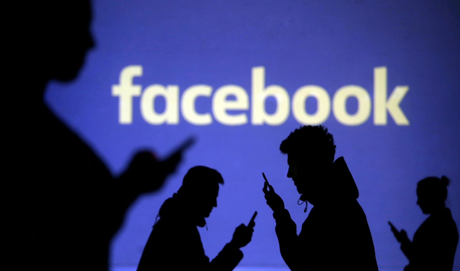 Silhouettes of mobile users are seen next to a screen projection of Facebook logo in this picture illustration taken March 28, 2018.Dado Ruvic / Reuters file