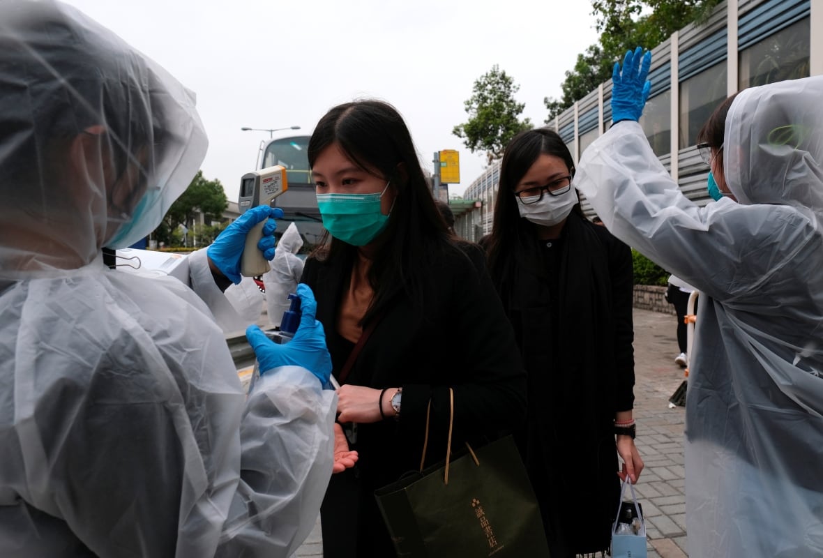 Residents wearing masks and raincoats volunteer to take the temperatures of passengers at a bus stop at Tin Shui Wai, a border town in Hong Kong, on Tuesday. Everyone entering Hong Kong from mainland China will soon be subject to a 14-day quarantine. (