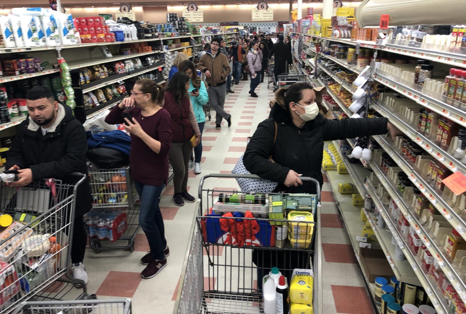 A woman in a protective mask shops as a line of shoppers stretch to the back of the store waiting to check-out at the Market Basket in Chelsea, MA on March 13, 2020. Bill Greene | Boston Globe | Getty Images