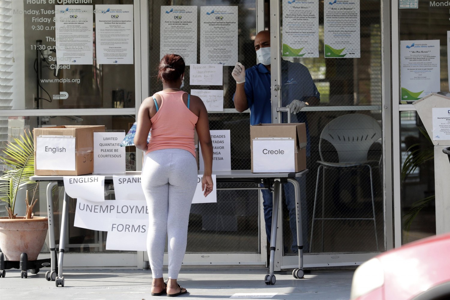 Harry Varela, right, wears a protective mask as he talks with a woman requesting an unemployment form at a Miami-Dade County library in Miami on April 8, 2020.Lynne Sladky / AP