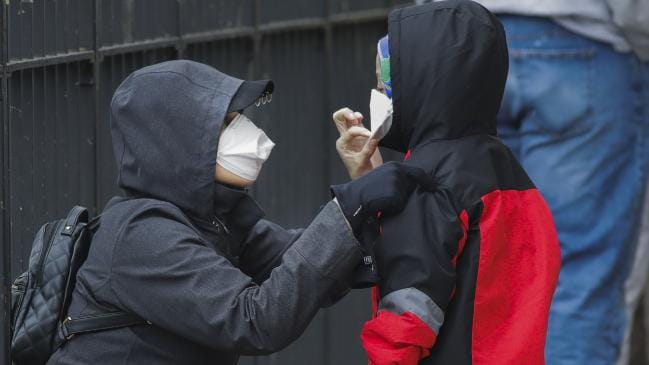 A woman adjusts her child's protective mask as they wait in line to be screened for COVID-19 at Gotham Health East New York.Source:AP