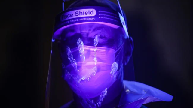 A St John Ambulance instructor is illuminated by ultra violet light to demonstrate how bacteria can spread as he trains volunteers to administer COVID-19 vaccines at Manchester United Football Club on January 30. Picture: Christopher Furlong/G