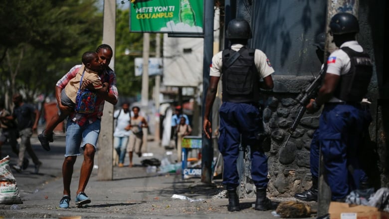 parent, carrying his child after picking him up from school, runs past police as they carry out an operation against gangs in the Bel-Air area of Port-au-Prince, Haiti on March 3. (Odelyn Joseph/The Associated Press )