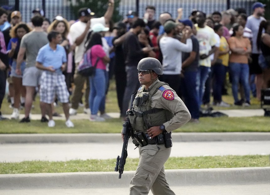 A law enforcement officer walks as people are evacuated from a shopping center where a shooting occurred Saturday in Allen, Texas. LM Otero / AP