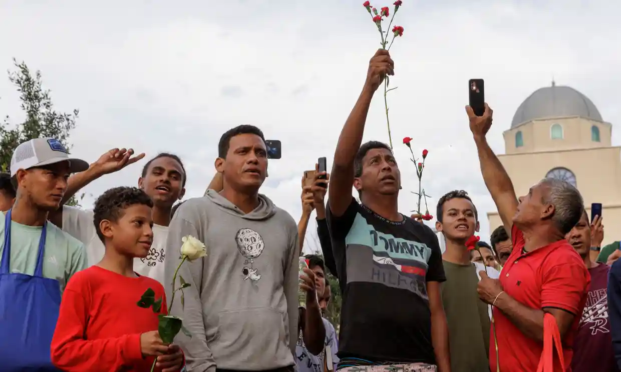 Migrants hold flowers during a vigil on Tuesday for the eight migrants who were killed the day before while waiting at a bus stop, in Brownsville, Texas. Photograph: Michael Gonzalez/AP