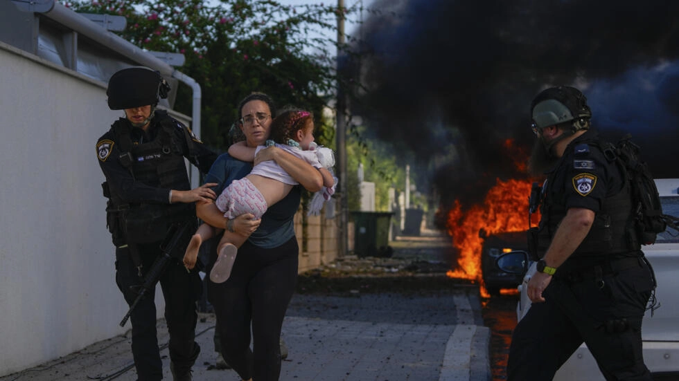 Police officers evacuate a woman and a child from a site hit by a rocket fired from the Gaza Strip in Ashkelon, southern Israel, on October 7. © Tsafrir Abayov, AP