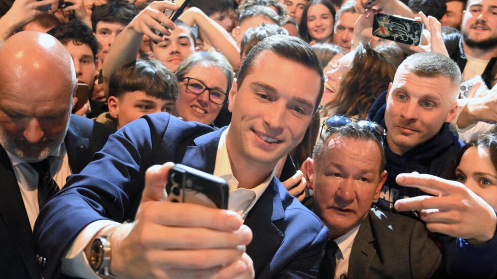 Jordan Bardella poses for a selfie with supporters during a campaign rally for the European elections in Montbeliard, eastern France, March 22, 2024. © Patrick Hertzog, AFP