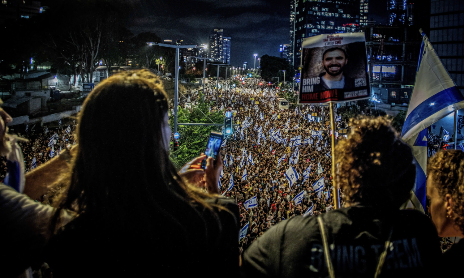 View image in fullscreen Protesters late on Sunday hold up placards and the Israeli flag during a demonstration in Tel Aviv. Photograph: Eyal Warshavsky/Sopa Images/Rex/Shutterstock