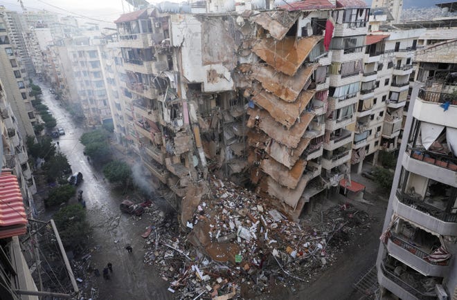 People walk past damaged buildings in the aftermath of Israeli strikes on Beirut's southern suburbs, on Nov. 25, 2024." data-c-credit="Mohammed Yassin, REUTERS