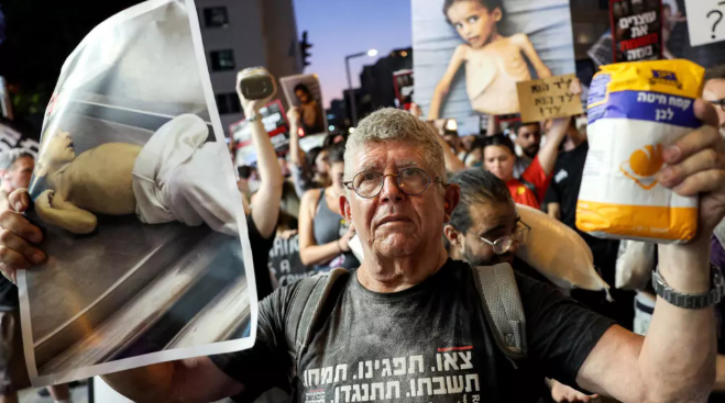 Un militant israélien tient un sac de farine et une photo d'un enfant souffrant de malnutrition lors d'une marche vers le siège du ministère israélien de la Défense à Tel-Aviv le 22 juillet 2025. © Jack Guez, AFP