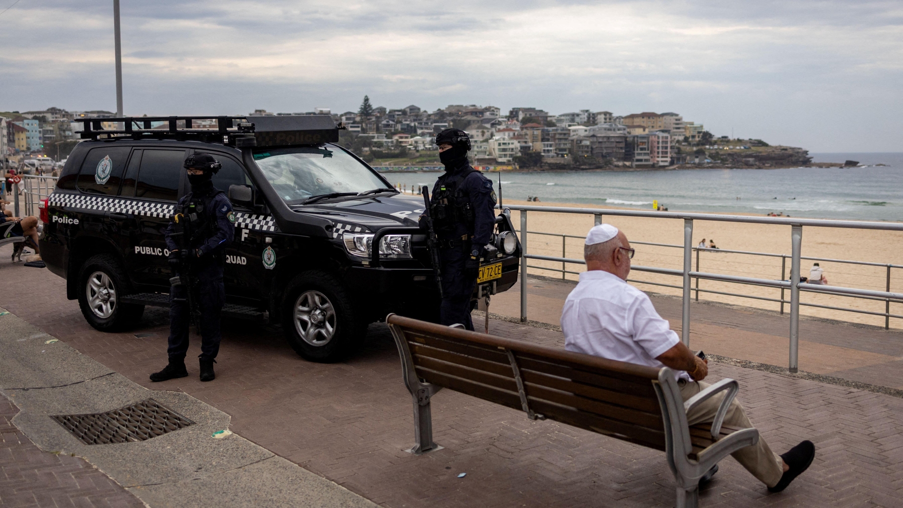 La police antiémeute reste en retrait, tandis qu'un homme juif est assis sur un banc à la plage de Bondi, à Sydney, en Australie, le 21 décembre 2025.  Photo : Reuters / Eloisa Lopez