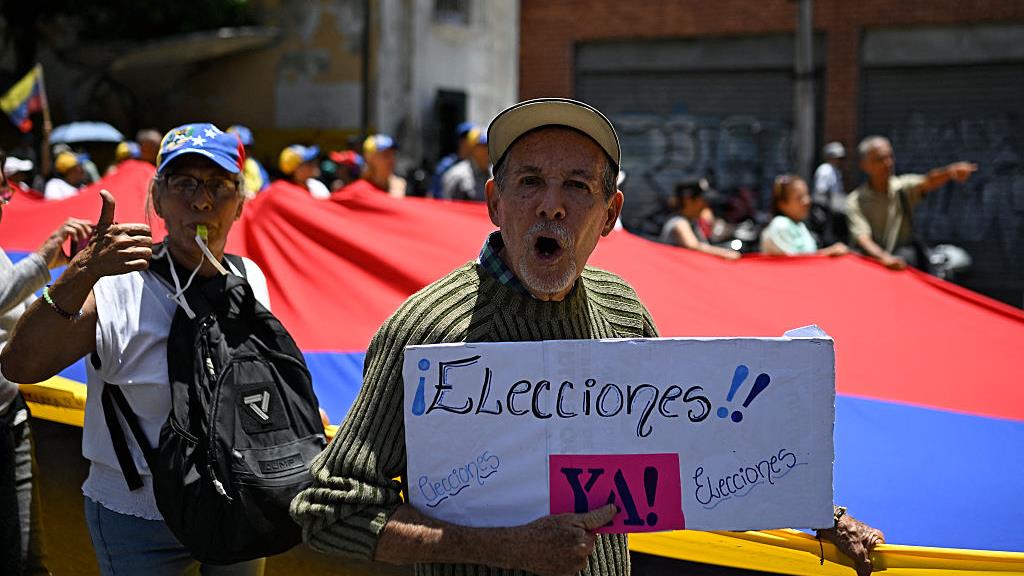 Des manifestants réclament la tenue d’élections, brandissant un grand drapeau national vénézuélien, à Caracas, le 28 juillet 2026.  Photo : Getty Images / FEDERICO PARRA / AFP