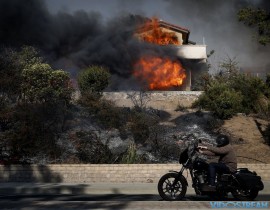 A man rides his bike past a home consumed by a wildfire on Dec. 5, 2017, in Ventura, Calif.